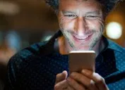 Closeup face of happy mature businessman messaging on cellphone at night on the street with the lights of the road blurred in the background.